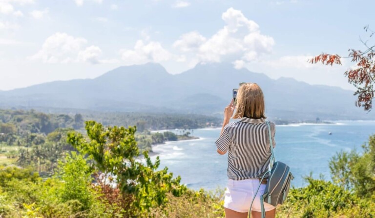 a woman taking a picture of the ocean with her cell phone
