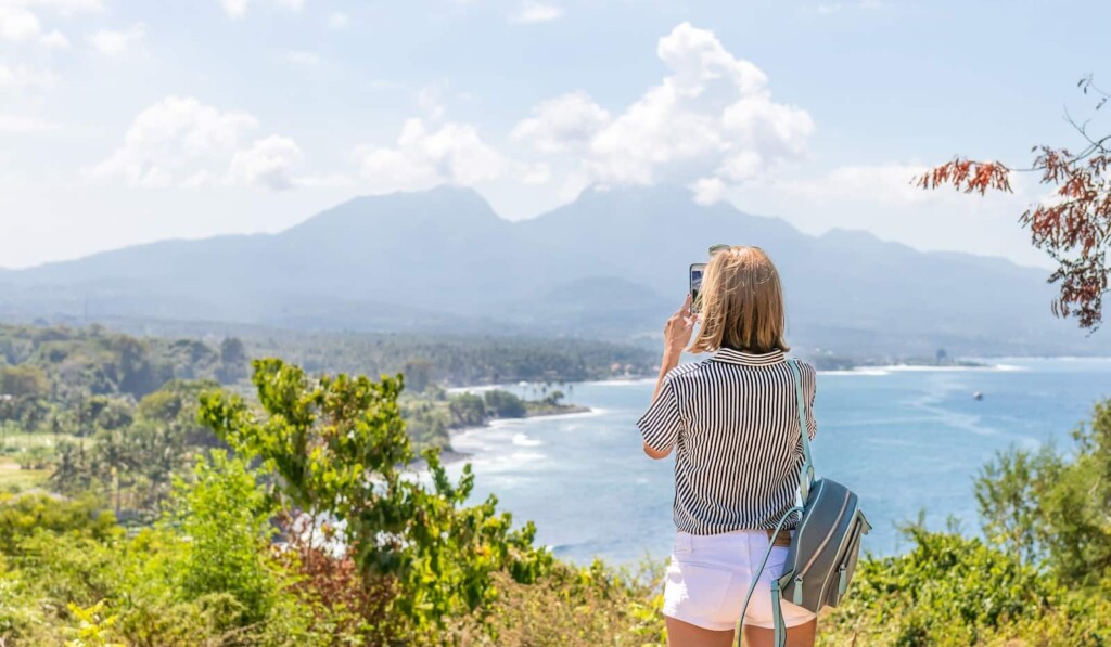a woman taking a picture of the ocean with her cell phone