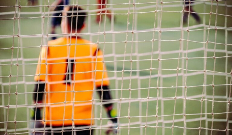 man in orange and black long sleeve shirt standing on soccer field