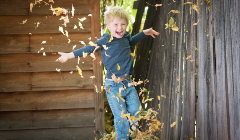 photo of boy near fence with falling leaves