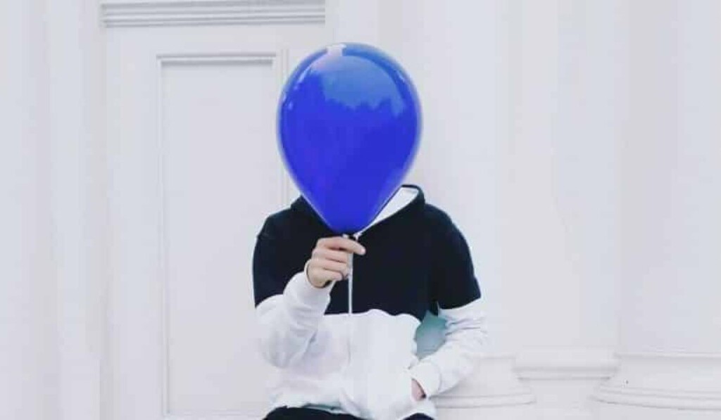 person sitting on white concrete pavement holding blue balloon at daytime